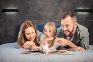 батьки з дитиною читають книгу разом лежачи на ліжку