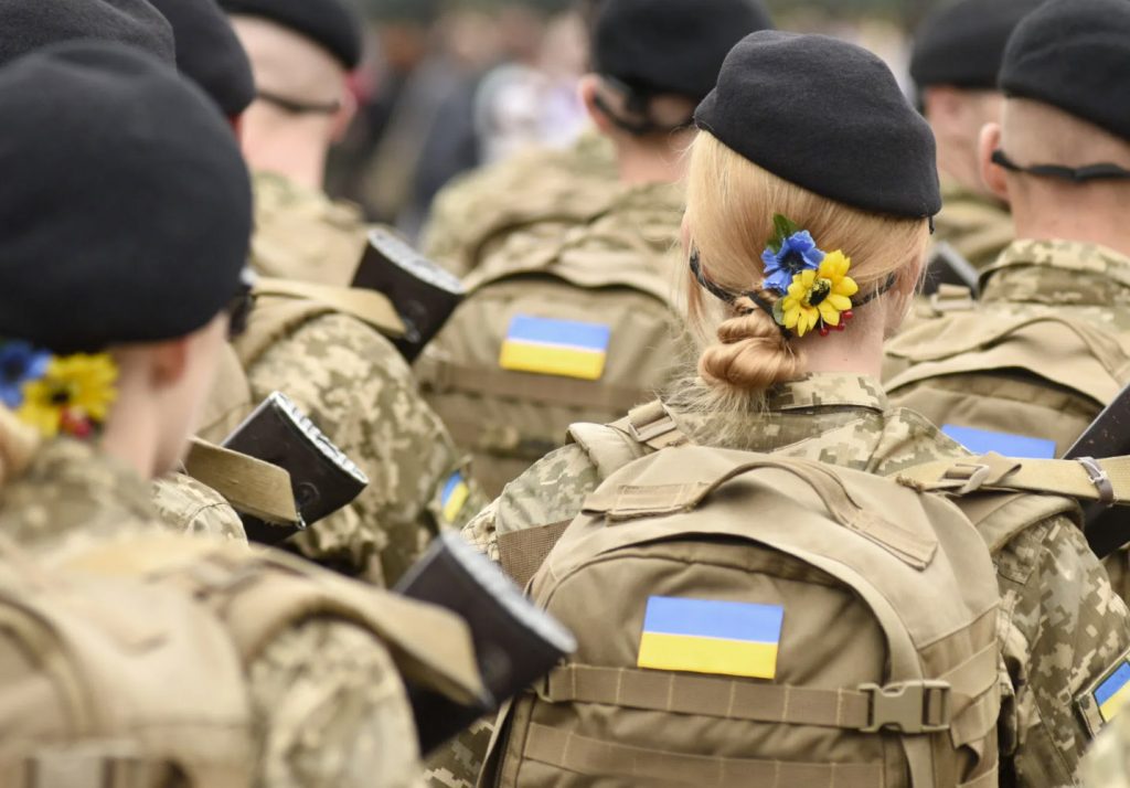 жінки-військові України у строю з прапорами на формі та квітами у волоссі