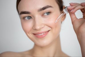 Нанесення сироватки для обличчя – жінка використовує піпетку для нанесення косметичної сироватки на чисту шкіру