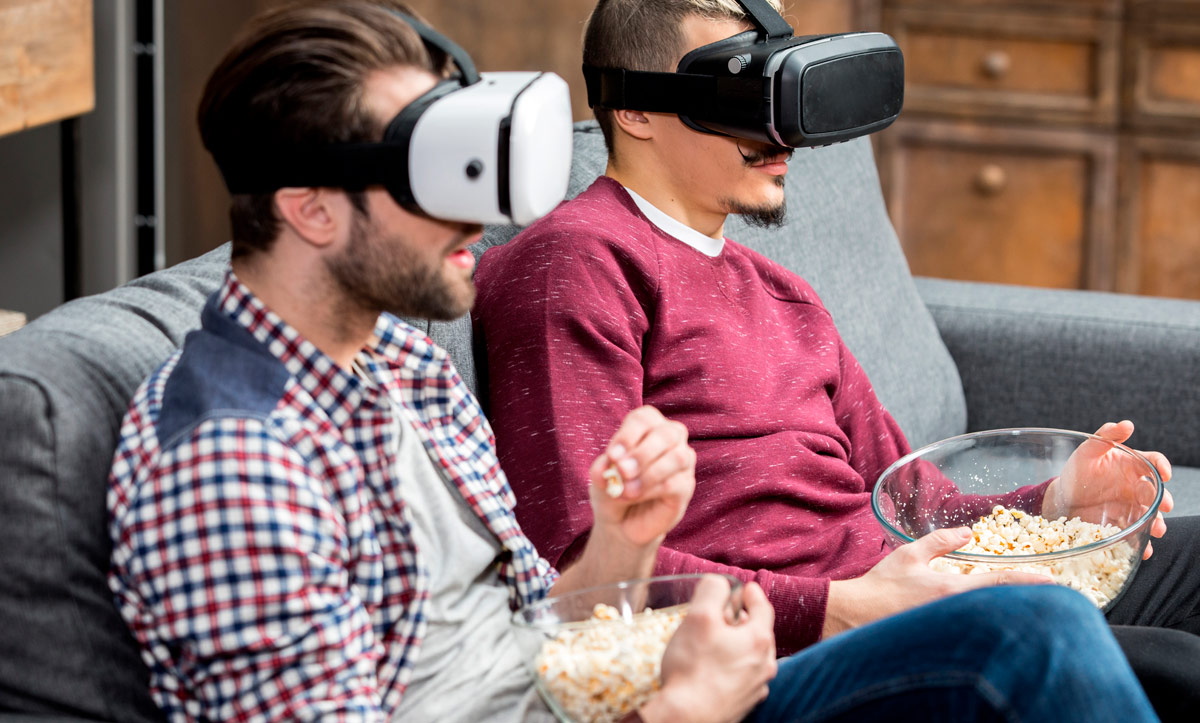 VR розваги вдома – двоє чоловіків у VR окулярах сидять на дивані та дивляться віртуальний контент, тримаючи попкорн